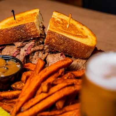 Brisket Melt with sweet potato fries and a side of bourbon mushroom sauce, close up.