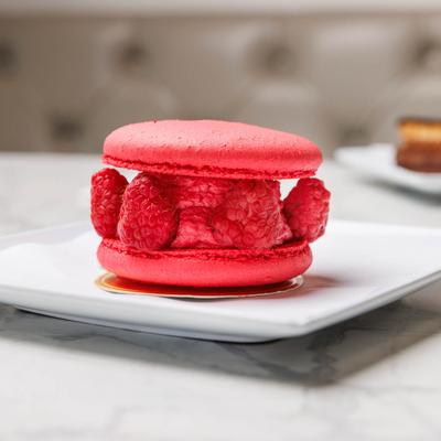Raspberry macaron with fresh raspberries on a white plate.