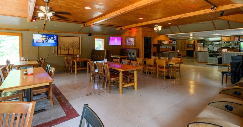 Interior - wooden tables, a ceiling fan, a TVs and a kitchen area in the background.