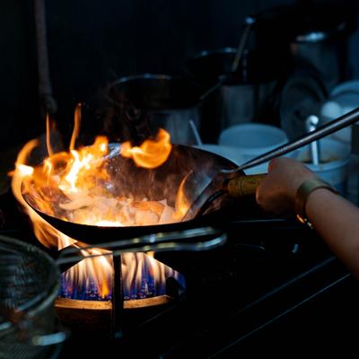 Chef cooking in a wok over a high-heat gas burner with active flame.