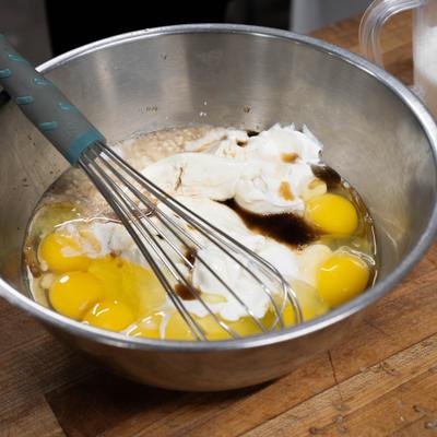 Eggs, flour, and sour cream in a mixing bowl with a whisker.