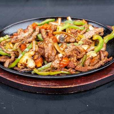 Steak fajitas served in a cast-iron skillet on a wooden base.