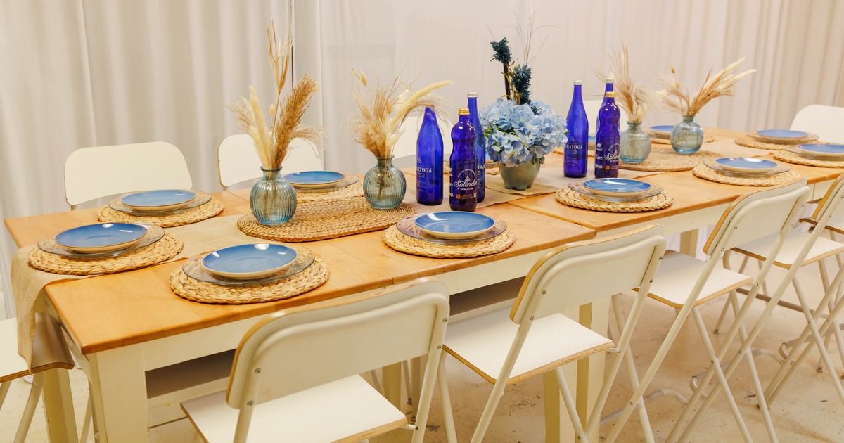 A dining table set for six with blue plates, dried pampas grass, surrounded by white chairs