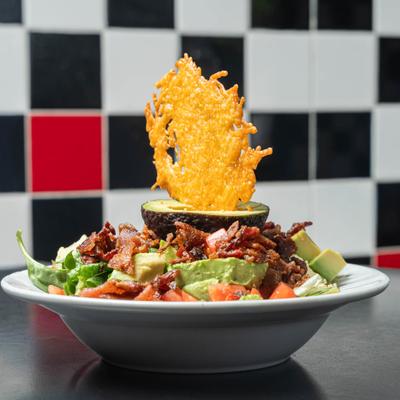 Keto Cobb salad with avocado, bacon pieces, diced tomatoes, greens and a cheese crisp.