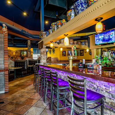 Bar area with high chairs, decorations and shelves with bottles.