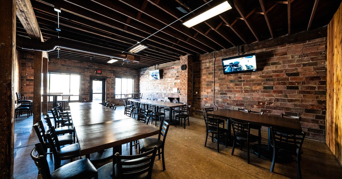 Spacious rustic room with brick walls, large wooden tables and  black chairs