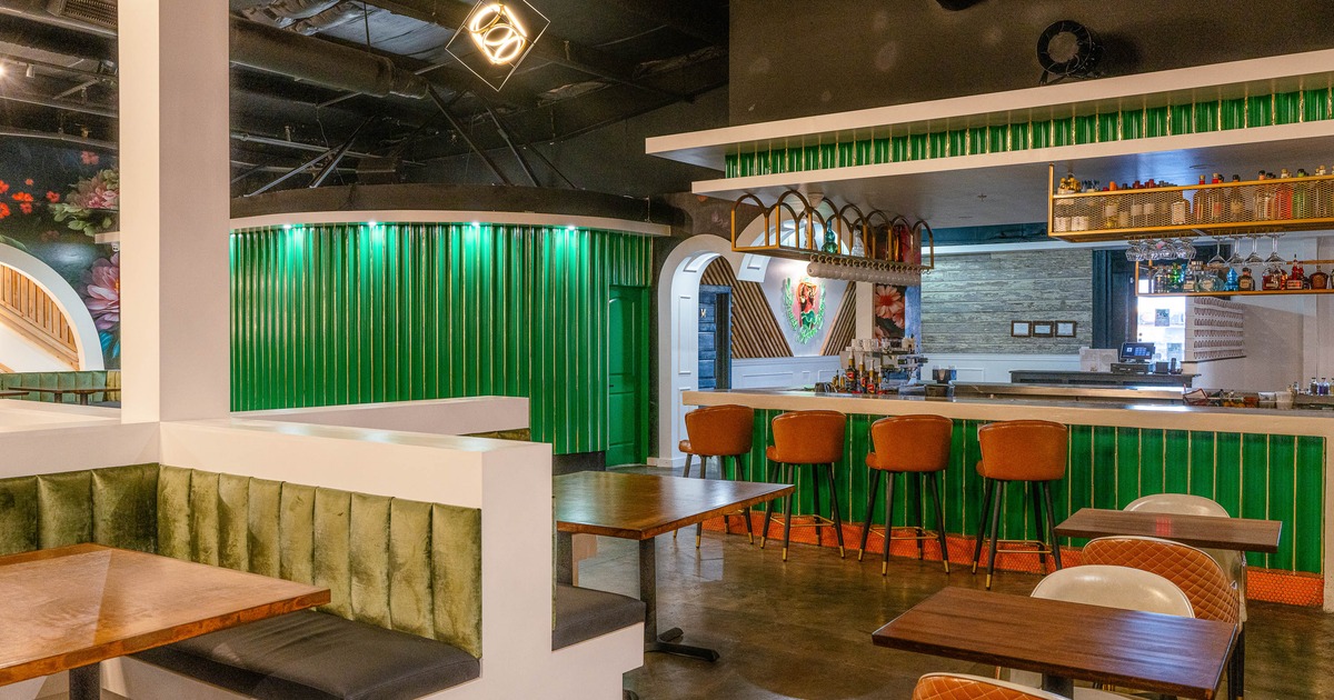 A modern interior - green accents, cushioned seating. Bar area with stools and liquor bottles.