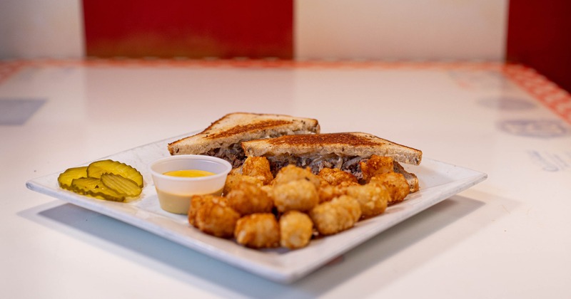 Toasted sandwich served with tater tots, pickle and sauce