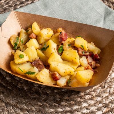 Bavarian Potato Salad served in a paper food tray with bacon and fresh herbs.
