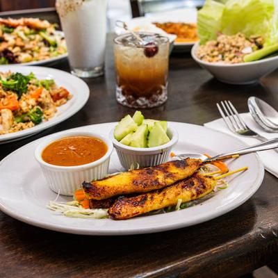 Chicken skewers served with peanut sauce, cucumber salad, and drinks.