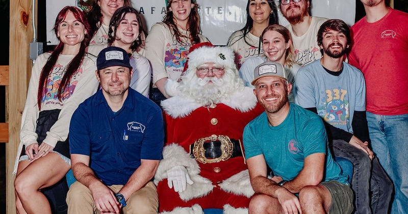 A group of smiling people posing with Santa Claus for a holiday picture indoors