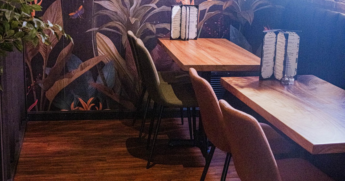 Cozy restaurant corner with tables, chairs, and a tropical mural on the wall.