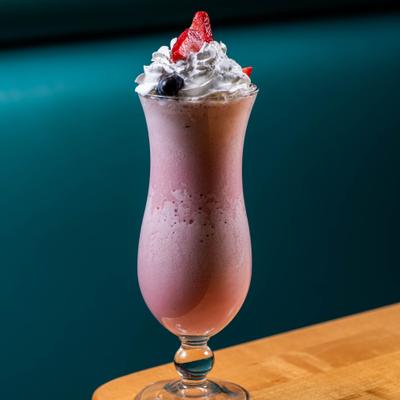 Strawberry Shake served in a traditional hurricane glass, garnished with whipped cream and berries.