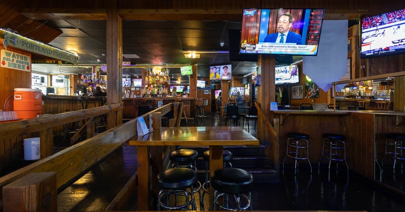 Interior of a wooden bar with tables, stools, a bar counter, and several TV screens