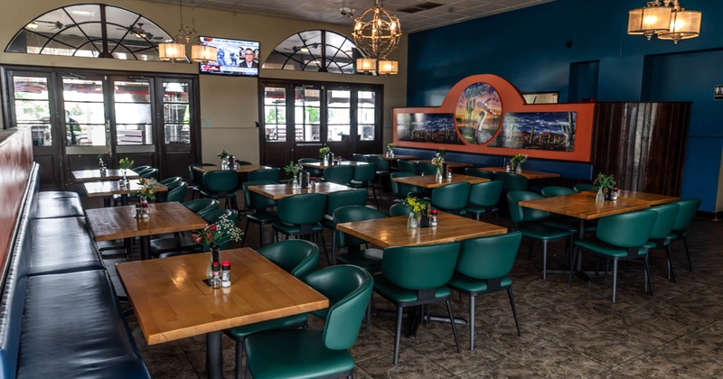 Interior, spacious restaurant with wooden tables, teal chairs, booths, pendant lights, wall artwork
