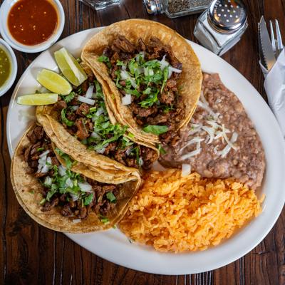 Beef tacos with cilantro and onions, served with Mexican rice, refried beans, and lime wedges.