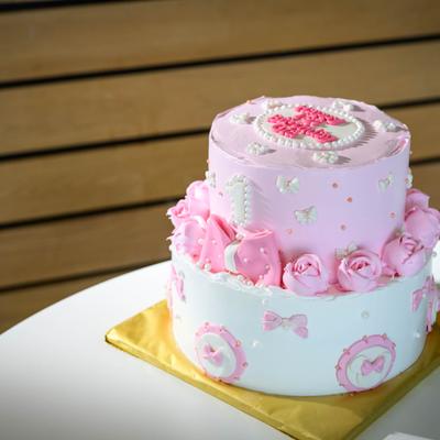 Two-tier pink and white first birthday cake with frosted roses and bows.