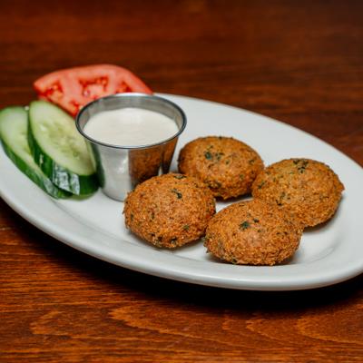 Falafel patties served with cucumber and tomato slices and tahini.