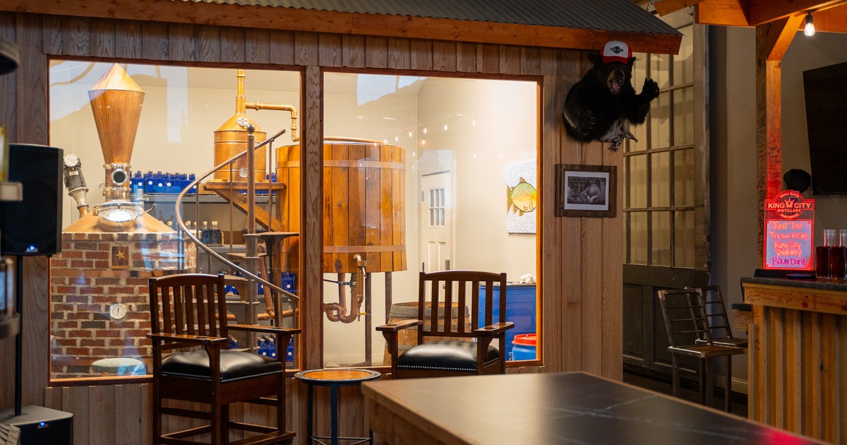Two upholstered chairs and a table, view of a distillery room behind the glass