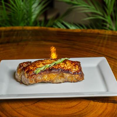 NY strip steak served on a white plate, topped with a rosemary sprig.