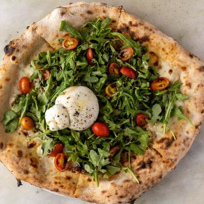 Pizza topped with arugula, cherry tomatoes and a ball of burrata cheese.