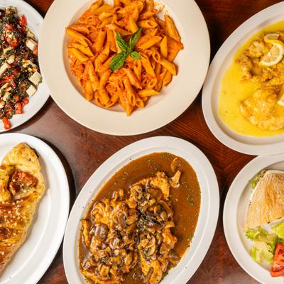 Plates of pasta, chicken, and salad on a wooden table.