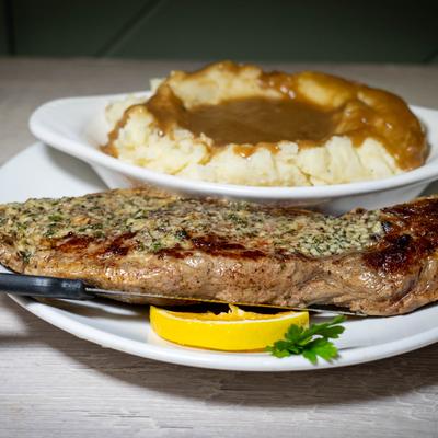 Grilled steak with herb butter, mashed potatoes, gravy, and lemon garnish.