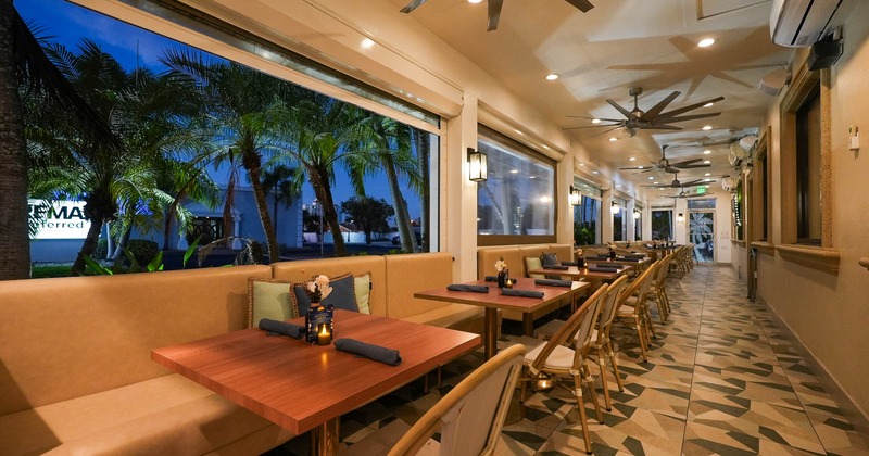 Interior - beige seating, wooden tables, large windows overlooking palm trees, patterned flooring