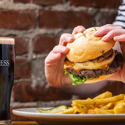 A person holds the times burger next to a pint of Guinness beer and a plate of french fries.