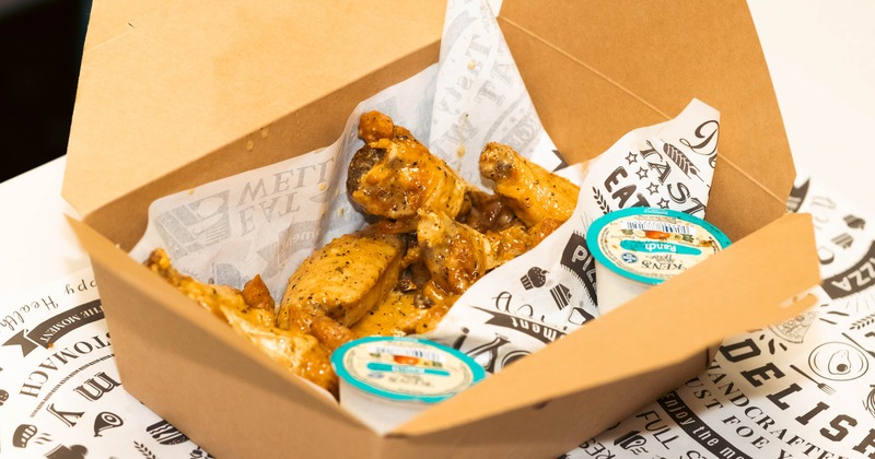 Chicken wings with dipping sauces inside a brown takeout box