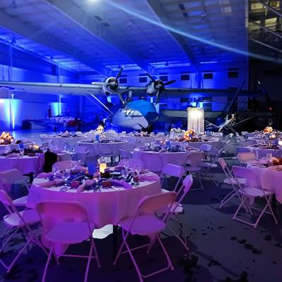 Airplane hangar event venue with banquet tables and blue lighting.