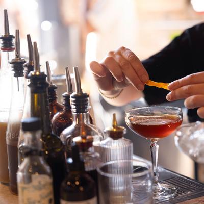A bartender preparing a cocktail and garnishing a red drink in a glass with an orange peel.
