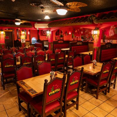 Restaurant interior with vibrant red decor, wooden tables, and chairs featuring fiesta logos.