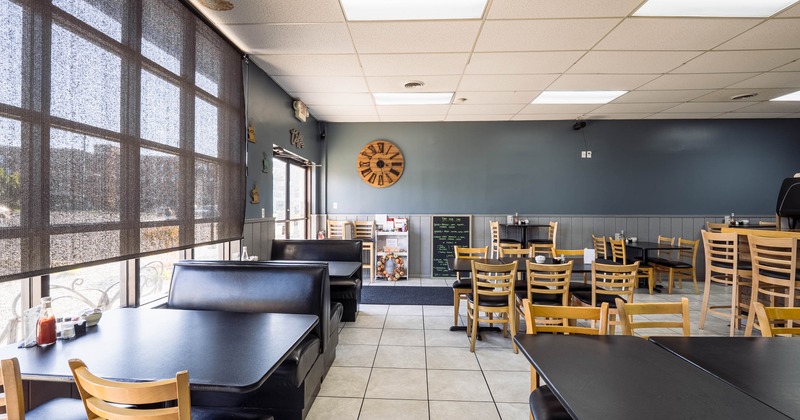 Interior of a restaurant with tiled floor, wooden chairs, black tables and booths
