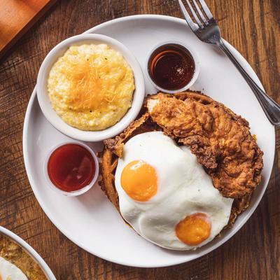 Chicken and waffles with two fried eggs, cheese grits, and dipping sauces