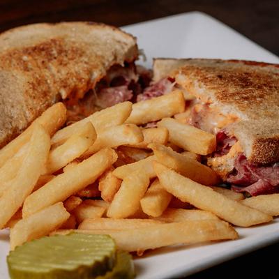 Grilled Reuben sandwich served with pickle and fries, close up.