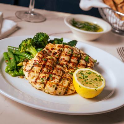 Grilled lemon chicken served alongside broccoli and a lemon half on a white plate.