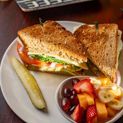 A club sandwich served with a pickle spear and fresh fruit bowl.