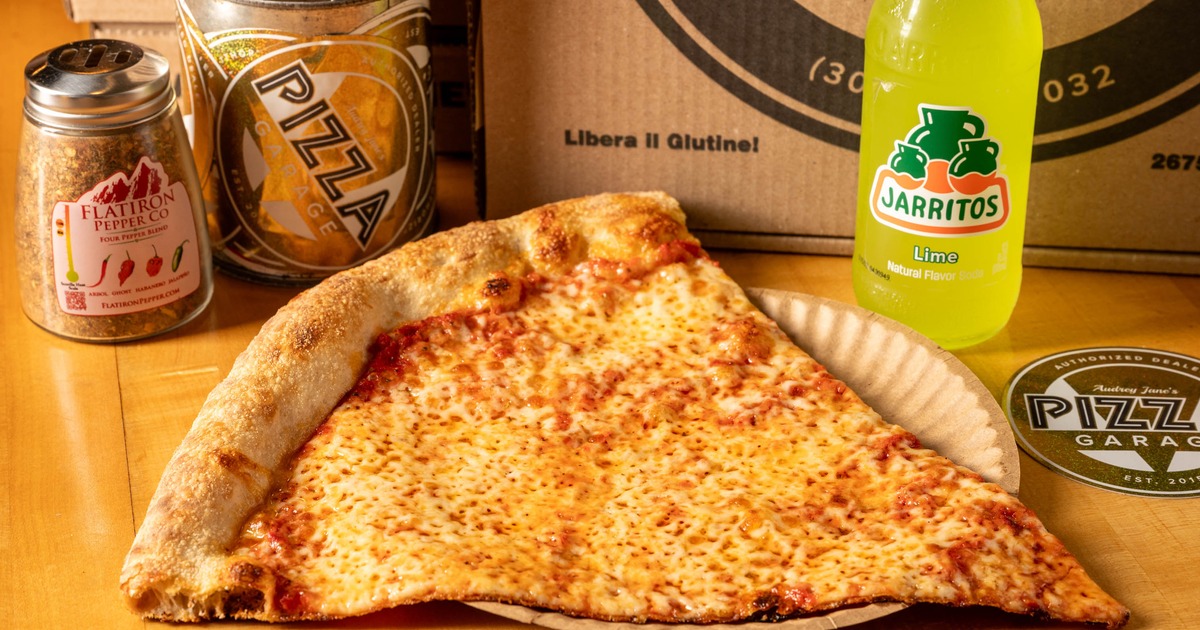 A large cheese pizza slice sits beside a Jarritos soda