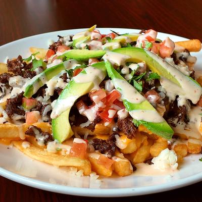 Steak fries topped with avocado slices, melted cheese, and creamy sauce.