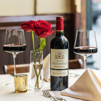 A table with two glasses of red wine, bottle of wine, and roses.