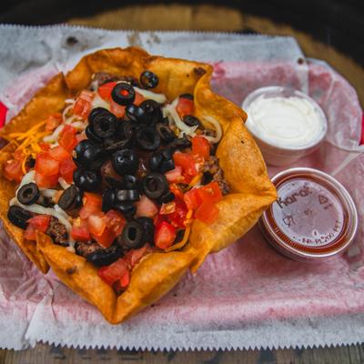 Taco salad served in a crispy tortilla shell and two cups of sauces, close-up.