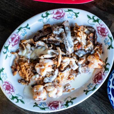 Grilled chicken, steak, and shrimp covered in cheese sauce, served over rice.