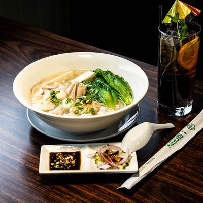 Noodle soup with meatballs and bok choy, served with condiments and a drink.