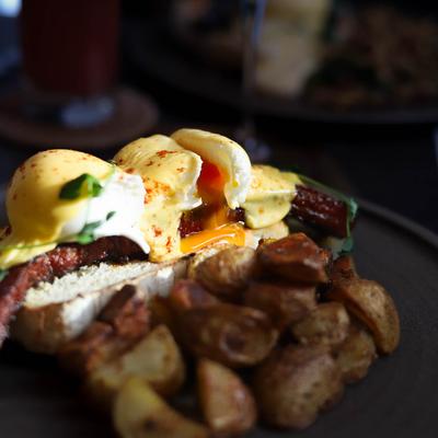 A close-up of poached eggs with hollandaise sauce, toasted bread, and roasted potatoes.