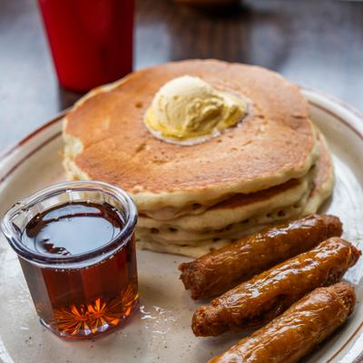 Stack of buttermilk pancakes with sausage links and maple syrup on a plate.