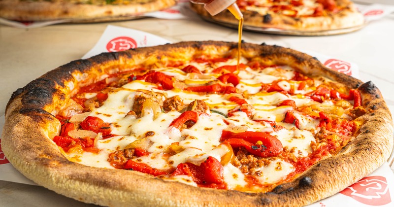 Hot honey being drizzled over a sausage pizza topped with red peppers