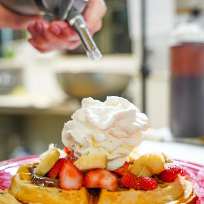Waffle with chocolate spread and fruit being topped with whipped cream.