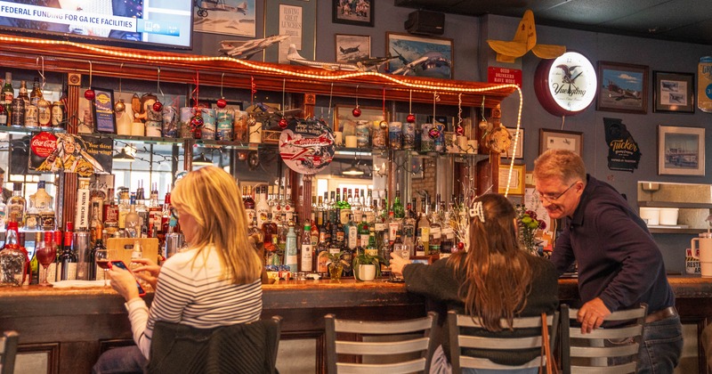 Bar area with shelving, aviation-themed decorations and guests seated at the counter