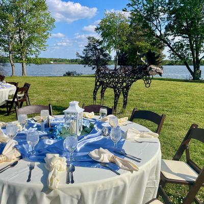 Outdoor wedding event table setup with a lakefront view and a decorative metal moose sculpture.